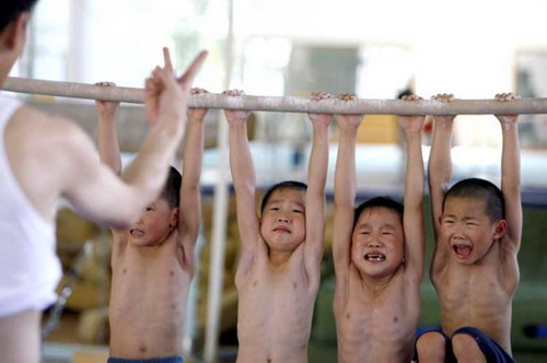 A coach counts down the time as boys hang on a bar for five minutes as part of a training session at the Gymnastics Hall of the Shanghai University of Sports