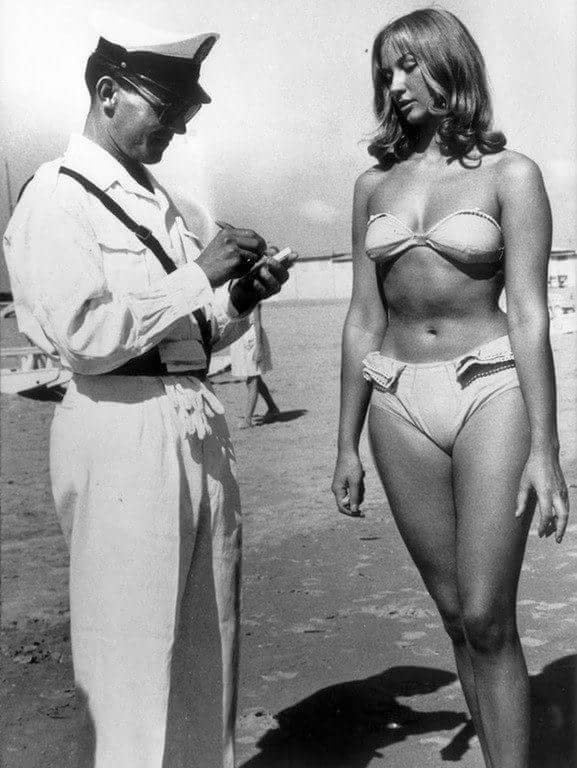 Полицейский улыбается и выписывает штраф женщине за ношение бикини на пляже, 1957 год, Римини, Италия